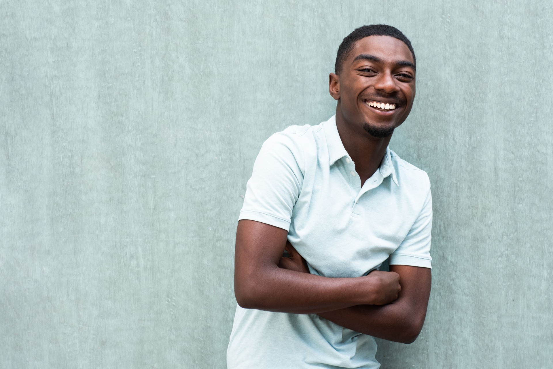 happy smiling young black man with arms crossed by wall